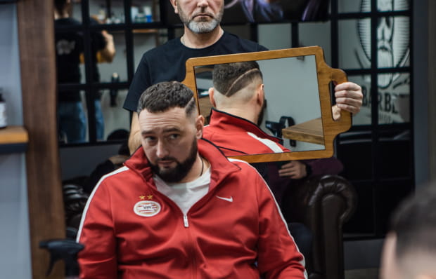 Мужчина в кресле барбершопа смотрится в зеркало